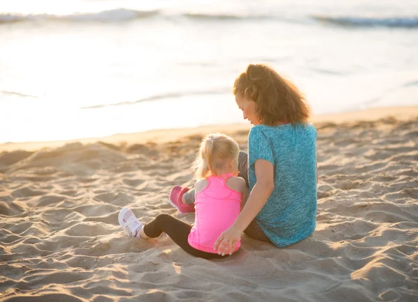 Young mother and daughter in workout gear sitting on beach — Stockfoto