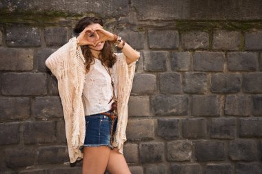 Longhaired hippy young woman near stone wall making heart hand
