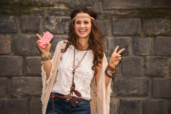 happy boho young woman near stone wall showing victory gesture