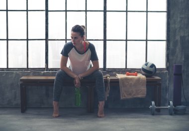 Woman resting elbows on knees while sitting on bench in loft gym