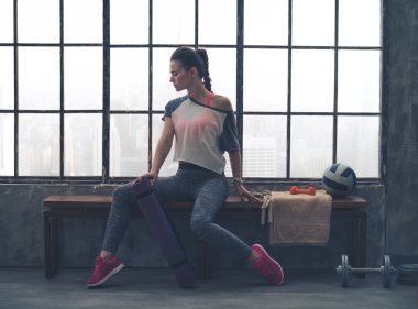 Woman in workout gear posing in profile on loft gym bench