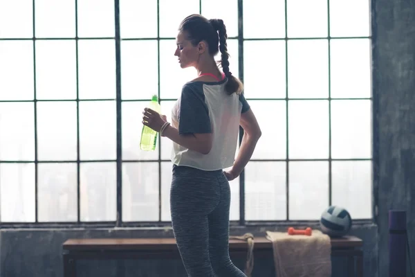 Profile view of fit woman holding water bottle in loft gym — 스톡 사진