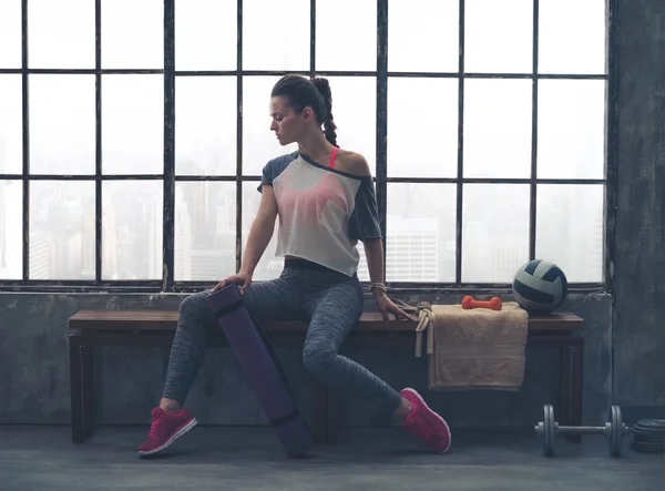 Woman in workout gear posing in profile on loft gym bench — 스톡 사진