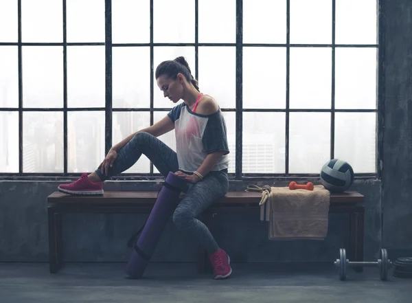 Fit woman in workout gear sitting on bench in loft gym — Zdjęcie stockowe