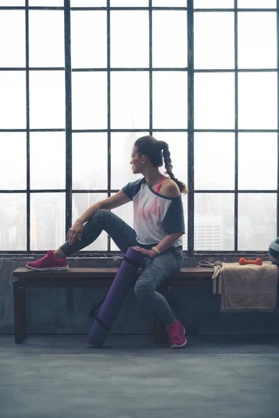 Fit woman sitting on loft gym bench looking out window — 스톡 사진