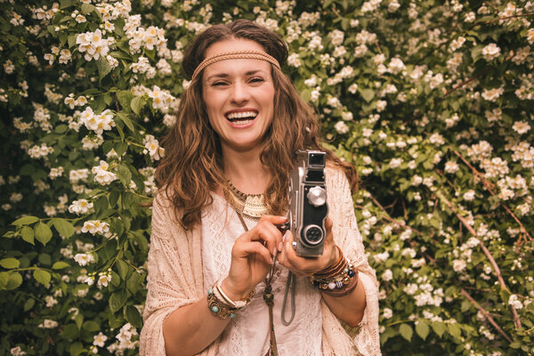 smiling boho young woman among flowers with retro camera