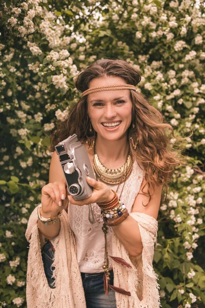 Lächelnde Hippie-junge Frau inmitten von Blumen mit Retro-Kamera — Stockfoto