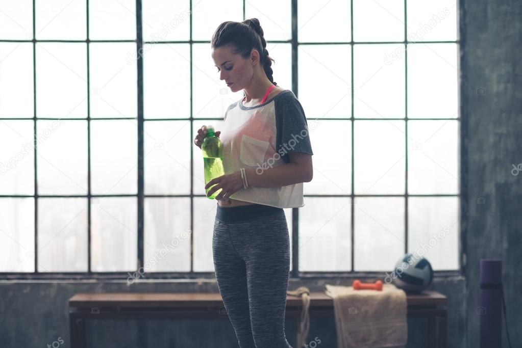 Fit woman standing in profile in loft gym holding water bottle