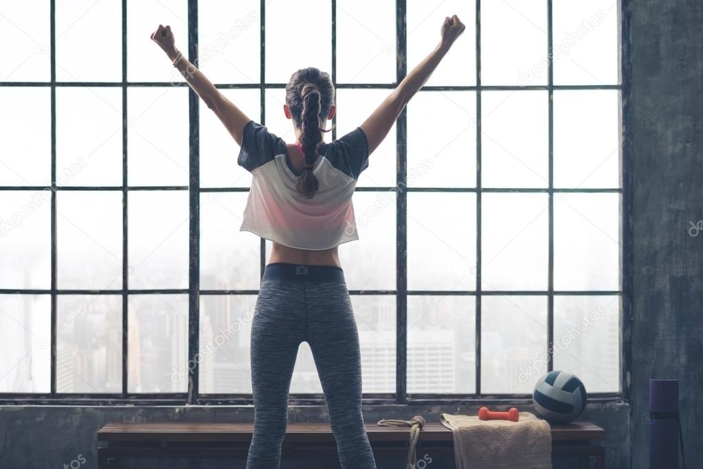 Rear view of rejoicing woman standing by window in loft gym