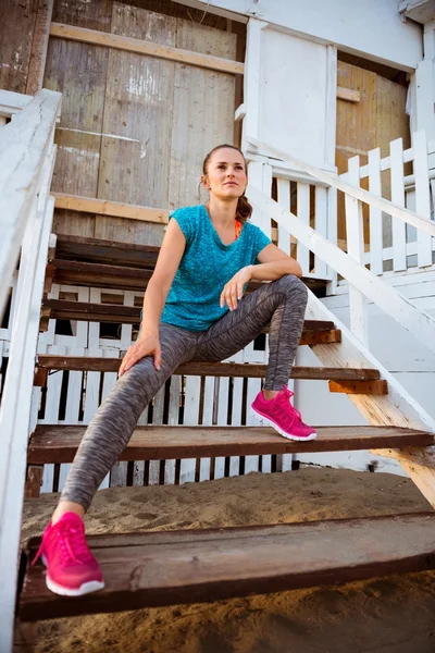 Woman runner sitting on wooden steps of a beach hut — Stockfoto