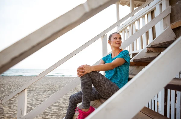 Woman in fitness gear relaxing on beach house steps — Stock Photo, Image