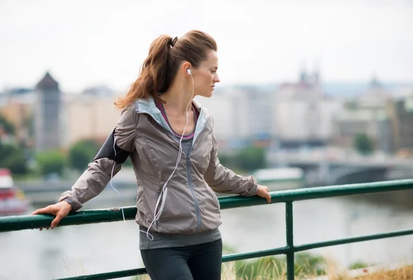 Woman runner with headphones in profile, up against guardrail