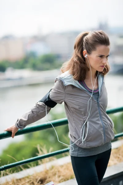 Woman runner stretching using a guardrail and listening to music — Stock Photo, Image