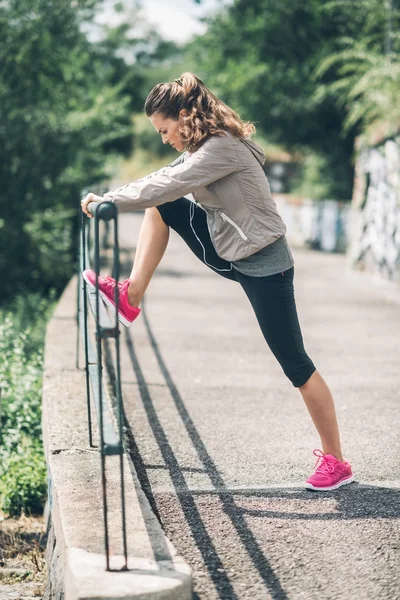 An athletic woman in profile stretching out against guardrail — Stock Photo, Image