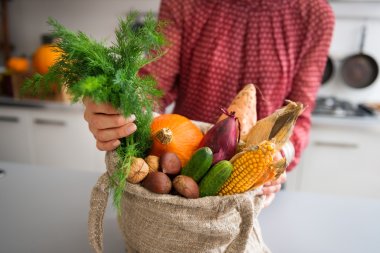 Closeup of fall vegetables and nuts in burlap bag held by woman