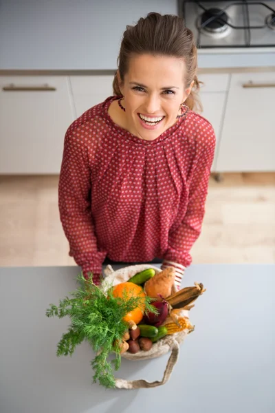 Donna felice in cucina guardando in alto tenendo sacchetto di verdure autunnali — Foto Stock