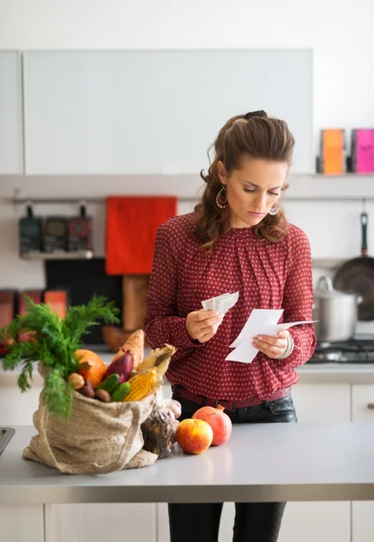 Mulher elegante em pé na cozinha segurando lista de compras e dinheiro — Fotografia de Stock