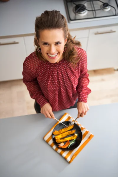 Sorrindo mulher olhando para cima na cozinha cortando legumes assados — Fotografia de Stock