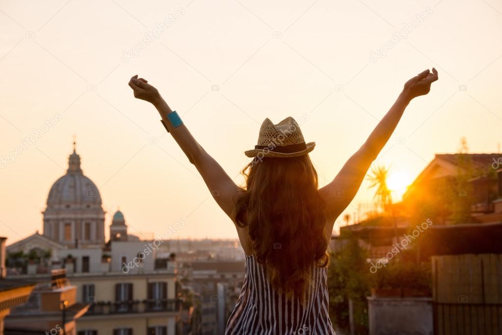 Woman from behind with outstretched arms in Rome at sunset