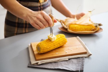 A woman's hand putting butter on corn on the cob on board