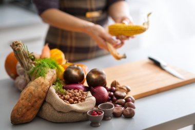 Autumn vegetables in a kitchen with anonymous woman husking corn