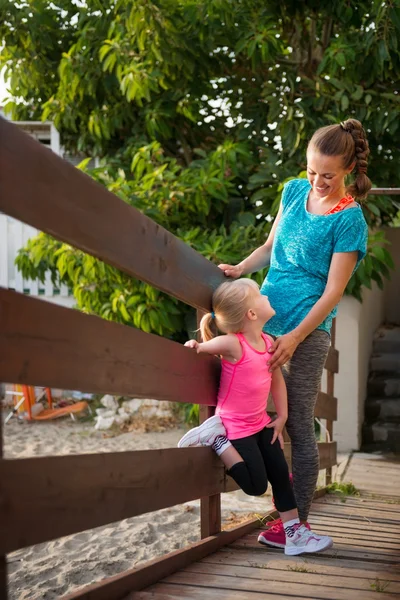 Young mother and daughter standing on a wooden bridge on beach — Stock Photo, Image