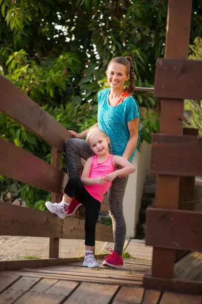 Glückliche junge Mutter und Tochter stehen auf Holzbrücke am Strand — Stockfoto
