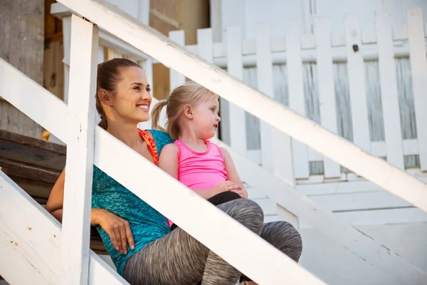 Smiling mother in profile on beach house steps with child — Stock Photo, Image