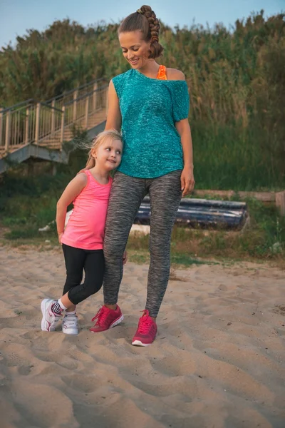 Happy mother and daughter in fitness gear standing on beach — Stock Photo, Image