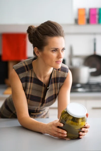 Elegant woman leaning on kitchen counter holding jar of pickles — Φωτογραφία Αρχείου