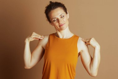 Gözleri ve kafası kapalı bir kadın, omuzlarına nazikçe masaj yapar, hardal atlet bluzunun içinde, yumuşak kahverengi bir stüdyo arka planına karşı rahatlık ve stres giderici bulur..