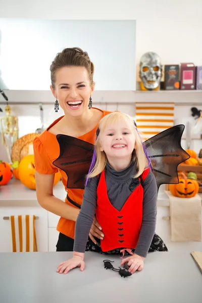 Chica feliz en traje de murciélago de Halloween con madre en la cocina — Foto de Stock