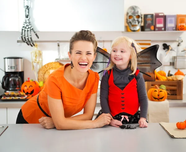 Chica divertida en traje de murciélago de Halloween con madre en la cocina —  Fotos de Stock