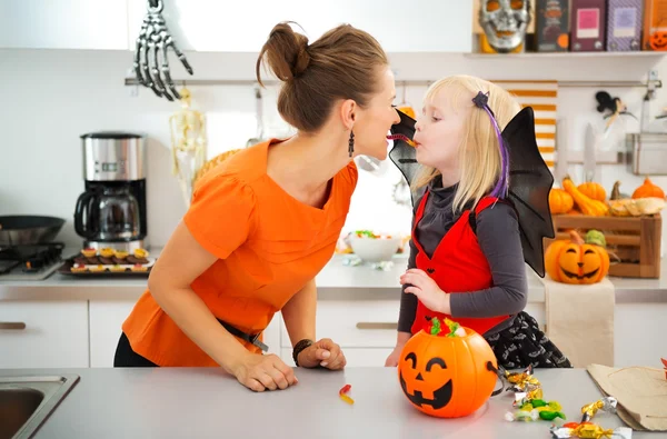 Divertida madre con hija en traje de murciélago comiendo caramelos de Halloween —  Fotos de Stock