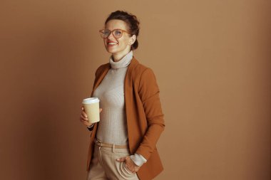 Hoş bir iş kadını, zarif bir ceket ve gözlük giymiş, bir kahve fincanı tutuyor, yoğun iş gününde özgüven ve düşüncelilik yayıyor..