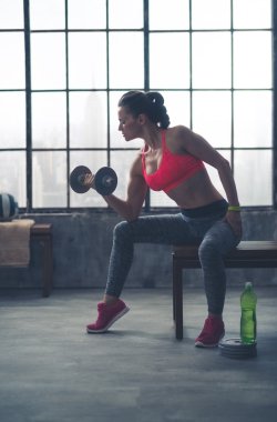 Çatı katında spor salonunda ağırlık profilde bankta oturan kadın