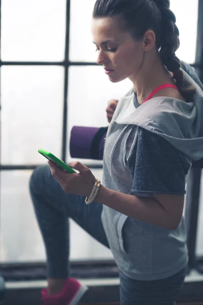 Fit vrouw in uitoefening versnelling in loft sportschool kijkt neer op telefoon — Stockfoto