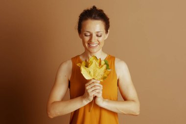 Huzurlu bir gülüşü ve kapalı gözleri olan bir kadın küçük bir buket sonbahar yapraklarını nazikçe tutar, huzurlu bir neşe yayar ve doğaya derin bir şükran duyar..