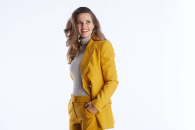 Dalgalı kahverengi saçlı, hardal sarısı takım elbiseli, gri balıkçı yakalı, kendine güvenen profesyonel bir kadın, beyaz stüdyo arka planına el ele bakarken gülümsüyor.