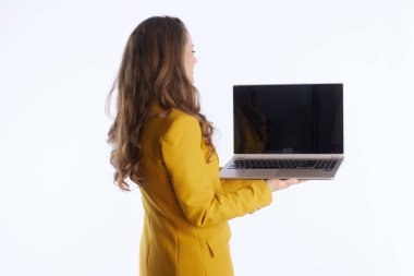 Açık gümüş dizüstü bilgisayara odaklanmış, parlak sarı ceketli profesyonel bir kadın arkadan ve yandan görülüyor. Bu benzersiz perspektif, konsantrasyon ve modern çalışma alanı bağlantısını vurgular