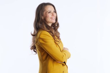 Neşeli bir ifadeyle profesyonel bir kadın, hardal sarısı bir ceket giyiyor, kollarını parlak beyaz bir stüdyonun arka planında kavuşturarak profilde duruyor..