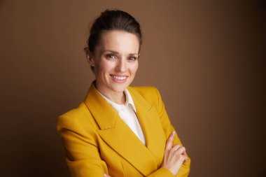 Sarı ceketli, gülümseyen bir iş kadını kahverengi bir arka plana karşı güven ve profesyonellik yayar. Kurumsal ve başarı temaları için mükemmeldir..