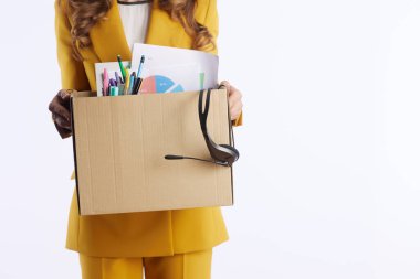 Sarı takım elbiseli bir kişi, ofis malzemeleriyle dolu bir karton kutu ve beyaz bir arka plana karşı bir kulaklık taşıyor. Bu da iş geçişini ya da ofis yerini değiştirmeyi simgeliyor..