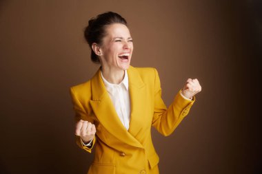 A joyful businesswoman in a yellow blazer celebrates with eyes closed and arms raised, embodying the triumph and excitement of significant achievement in her professional life.