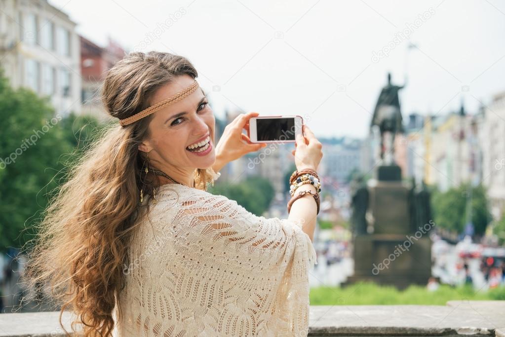 Trendy hippie woman tourist taking photo on mobile in Prague