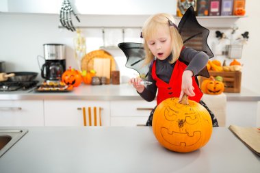 Halloween dressed girl creating pumpkin Jack-O-Lantern