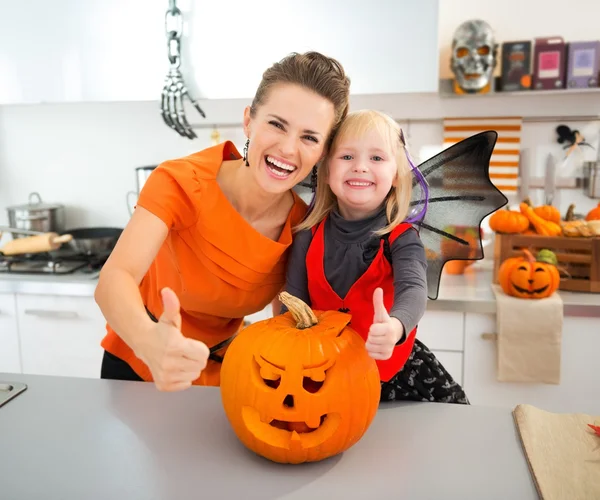 Halloween dressed girl with mother showing thumbs up in kitchen — Stockfoto