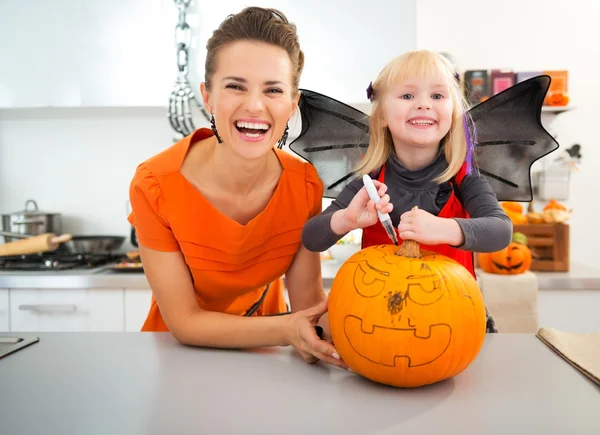 Mother with halloween dressed daughter creating Jack-O-Lantern — Stock Photo, Image