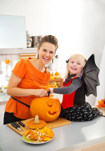 Mother with halloween dressed daughter carving Jack-O-Lantern — стокове фото