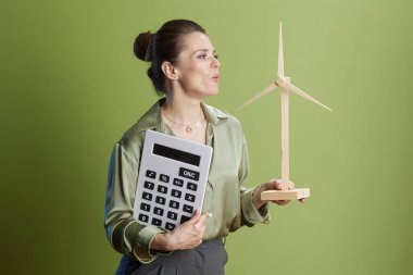 Bir kadın temiz enerjiye odaklanmış bir rüzgar türbini ve hesap makinesi tutuyor. Açık yeşil bir arkaplan, sürdürülebilirlik ve gelecekteki yatırımlar üzerine kurulur.